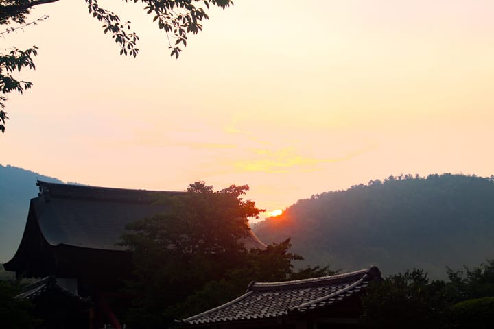 sun setting behind the mountains in the background with building in the foreground, thumbnail