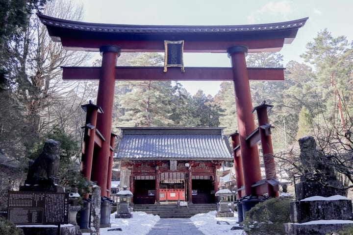 a tori gate that is painted red, with another gate in the background, two statues of lions on either side, thumbnail