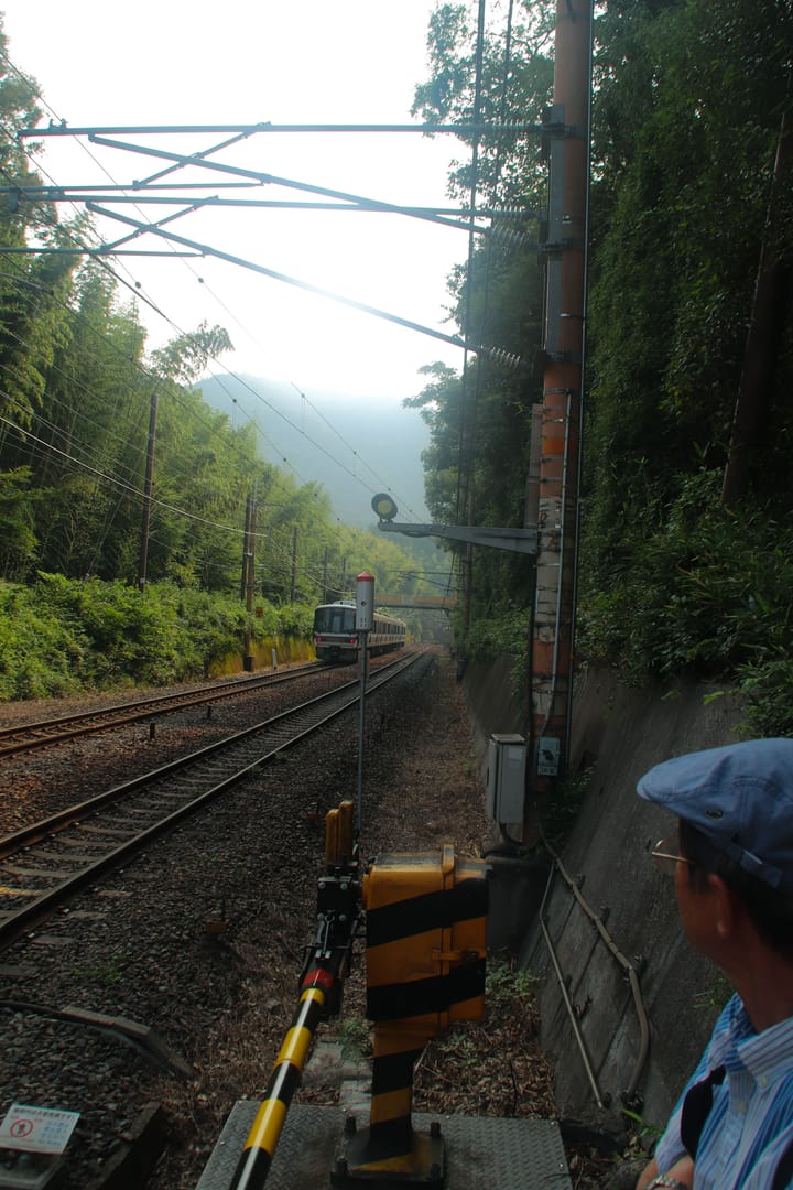 a train passing by as a man in a golf cap looks in its direction, thumbnail