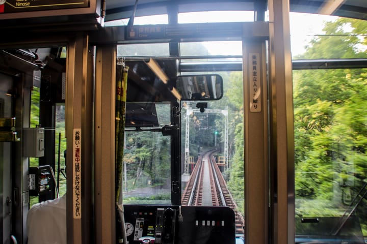 a view of the train tracks from the front of the train as it heads through a wooded area, thumbnail